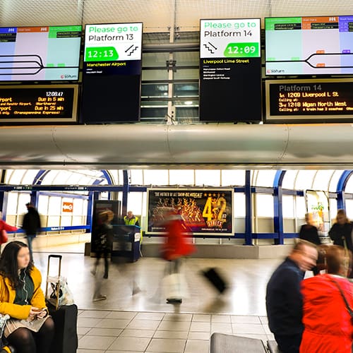 Digital signage screens showing passenger information at a train station in Manchester