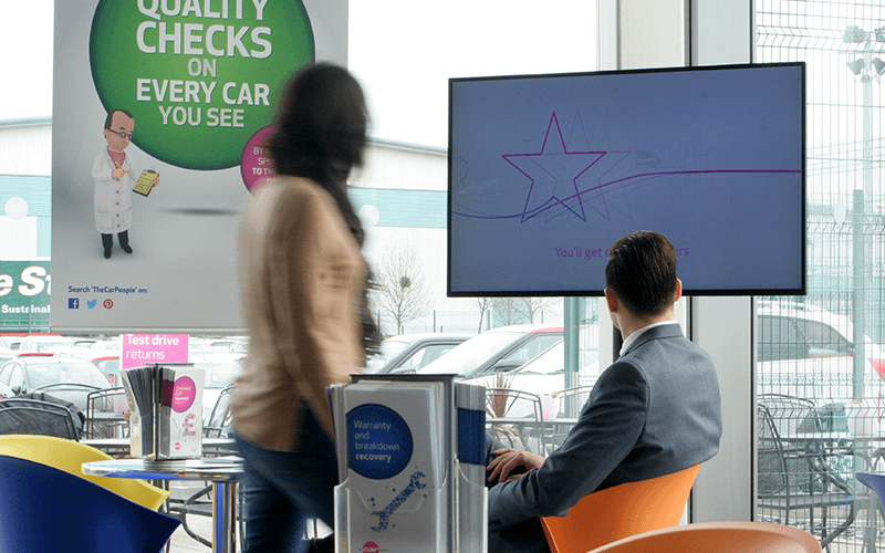 Man and a woman looking at digital signage in a car showroom