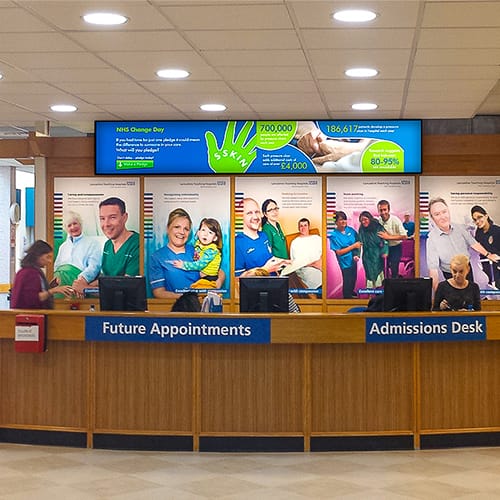 Digital signage screens at an admissions desk in a UK hospital