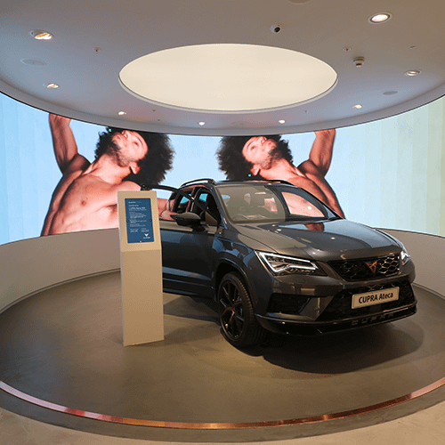 Cupra Ateca vehicle parked in front of a curved video wall in a car showroom