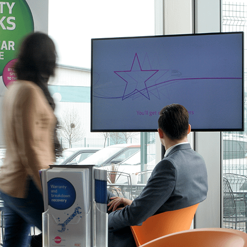 Corporate Digital Signage | A man and woman watching a video on digital signage screen in a car showroom