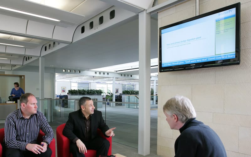 Men in an office looking at digital signage showing corporate communications channel