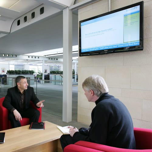 Men in an office looking at digital signage showing corporate communications channel